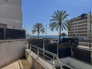 A coastal view with a parking area, palm trees, and a building with a balcony.