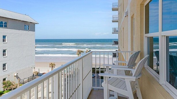 Een balkon met witte stoelen met uitzicht op een strand en oceaan.