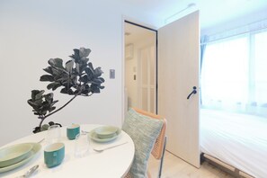 Una habitación con una cama, una mesa de comedor con platos y vasos, una silla y una planta.