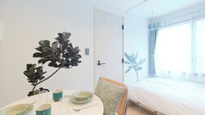 A room with a bed, a dining table with plates and cups, a chair, and a plant. - RIZOTIA HAKUSAN by Tranova (Tokyo)