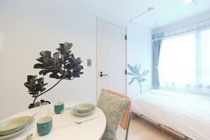 Una habitación con cama, una mesa de comedor con platos y tazas, una silla y una planta.