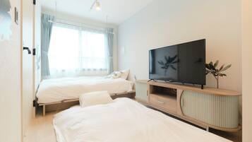 Una habitación de hotel moderna con dos camas individuales, televisión y un amplio ventanal con cortinas.