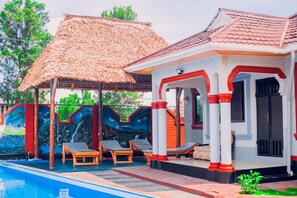 A pool area with lounge chairs and a thatched-roof structure. - Eagle Cottages (Moshi)