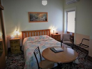 A cozy room with a bed, two bedside tables with lamps, a chair, and a small round table. - Sonbern Lodge Motel (Wallaroo)