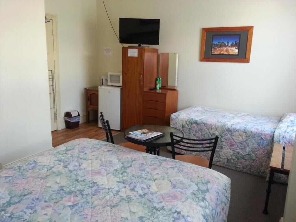 A room with two beds, a small table, a TV, a microwave, and a framed picture on the wall.