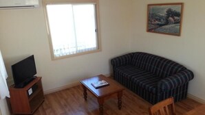 A living room with a plaid sofa, a wooden coffee table, a television on a stand, and a painting on the wall. - Sonbern Lodge Motel (Wallaroo)