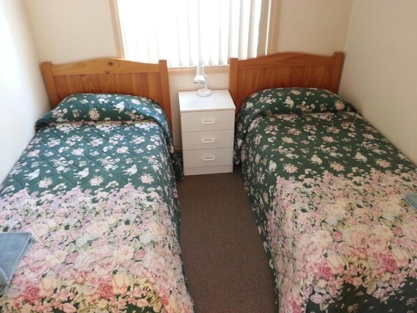 A bedroom with two single beds, a bedside table with a lamp, and a window with blinds. - Sonbern Lodge Motel (Wallaroo)