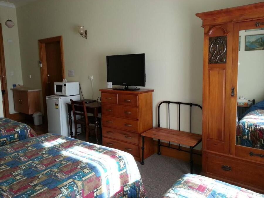 Un dormitorio con dos camas, un aparador, un escritorio con una computadora, un microondas y un televisor.