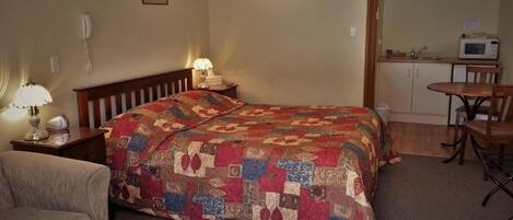 Een knus ingerichte kamer met een bed, een klein bureau, een lamp, een stoel en een magnetron.