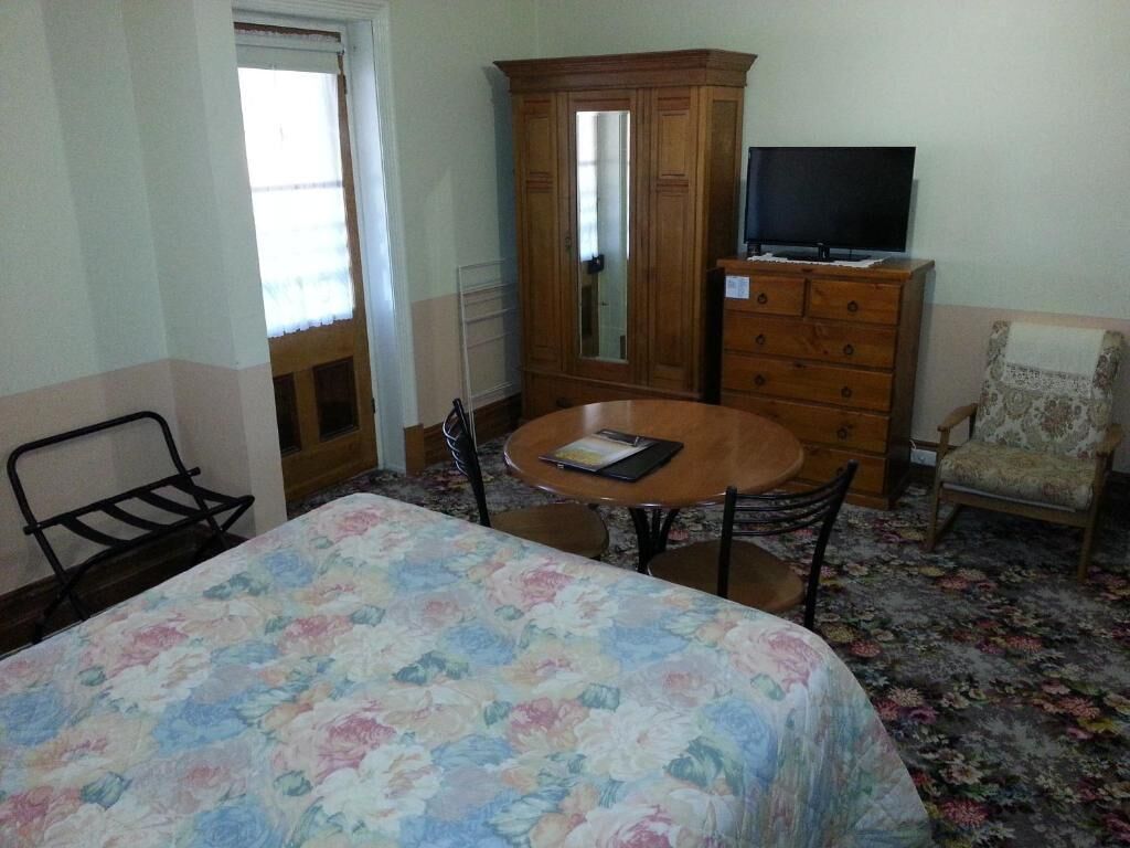 A hotel room with a bed, a wooden dresser, a television, a chair, and a round table.