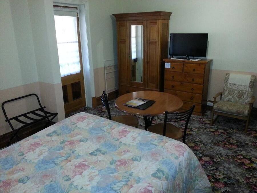 A hotel room with a bed, a wooden dresser, a television, a chair, and a round table.