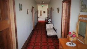 A hallway with patterned carpet, wooden doors, a bench, and a dresser with decorative items. - Sonbern Lodge Motel (Wallaroo)