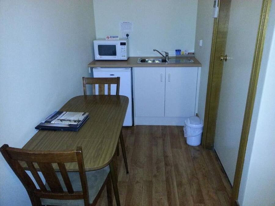 A compact kitchen with a microwave, sink, and cabinets. There is a dining table with chairs and a trash bin.
