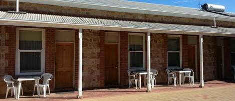 A building with a brick facade, multiple doors, and outdoor seating areas with tables and chairs.