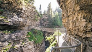 Eine Hängebrücke in einer Schlucht mit felsigen Klippen und Grünflächen.
