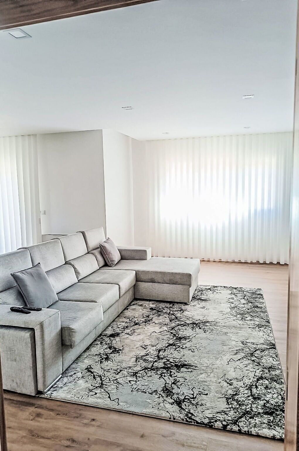 A modern living room with a grey sectional sofa, a patterned rug, and sheer white curtains.