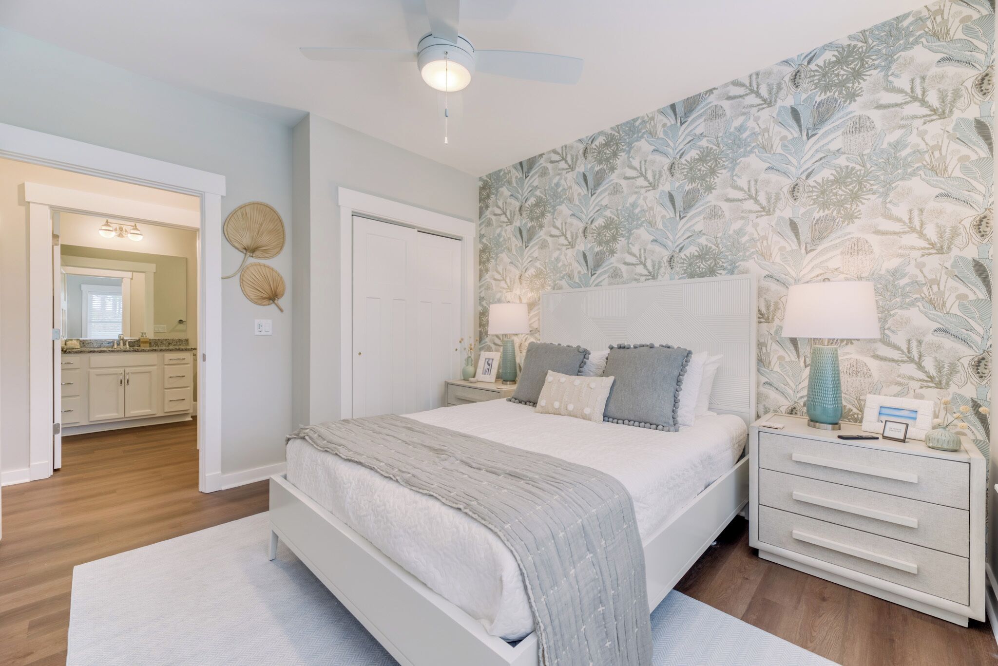 Un dormitorio con cama, mesitas de noche, ventilador de techo y papel tapiz floral.