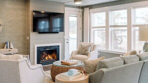 Un salon moderne doté d’une cheminée, d’un téléviseur à écran plat, d’un ventilateur de plafond et de grandes fenêtres.