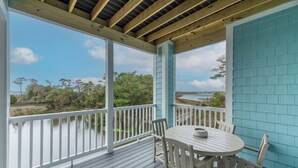 A covered outdoor area with a table and chairs, overlooking a body of water and greenery.