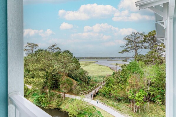 A view from a window overlooking a natural landscape with a wooden bridge, trees, and a body of water.