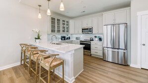 Une cuisine moderne avec des meubles blancs, des appareils en acier inoxydable et un îlot central doté de tabourets de bar.