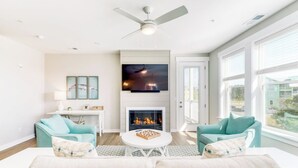 A modern living room with a fireplace, two teal armchairs, a white sofa, and a flat-screen TV mounted above the fireplace.