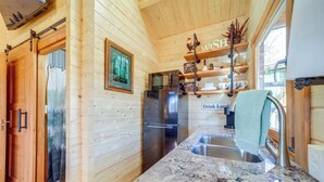 A wooden cabin interior with a kitchen featuring a stainless steel refrigerator, granite countertops, and a 'Drink Local' sign. - Charming 2-bedroom cottage with AC, WiFi in welcoming Waynesville (Waynesville)