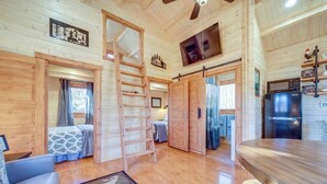 A cabin interior with a wooden floor, a ladder, a bed, a desk, and a refrigerator. - Charming 2-bedroom cottage with AC, WiFi in welcoming Waynesville (Waynesville)