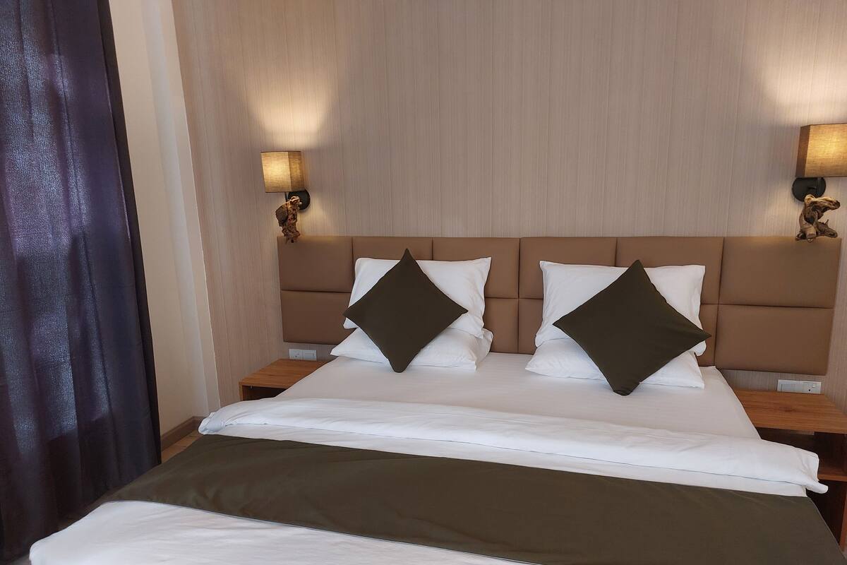 Une chambre d’hôtel avec un grand lit, deux tables de chevet et des lampes fixées au mur.
