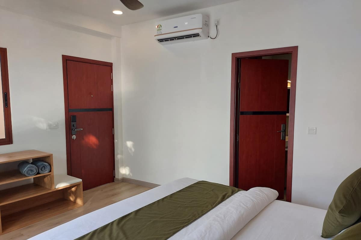 Une chambre d’hôtel avec un lit, une armoire en bois et une étagère où sont pliés les serviettes.