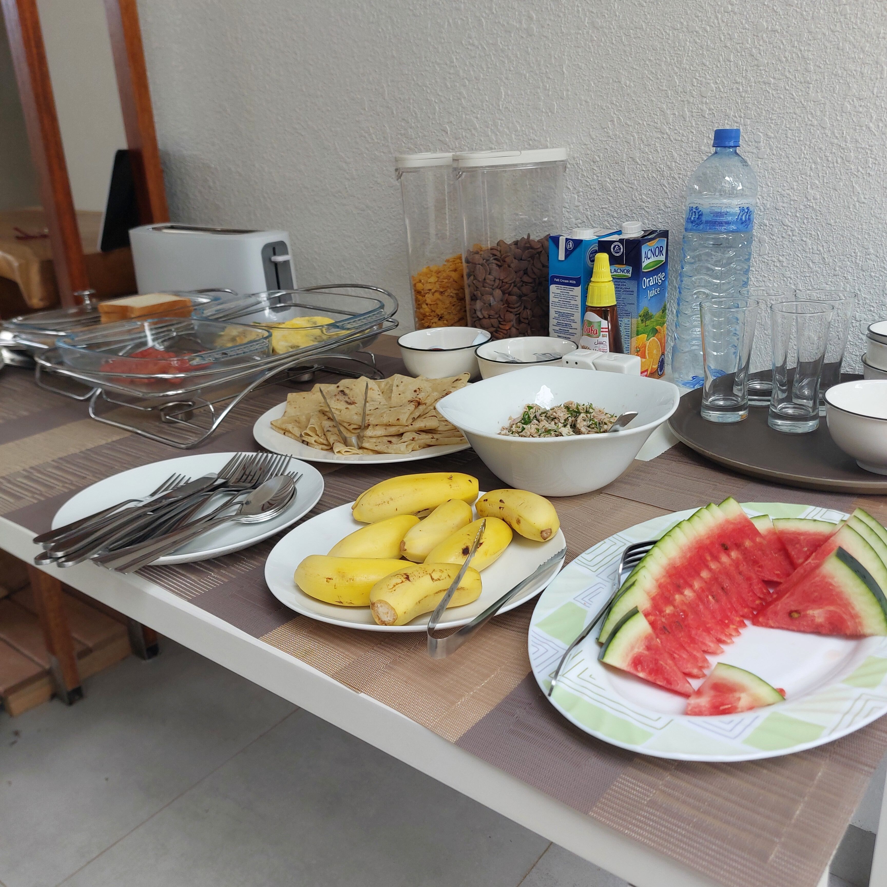A buffet table with various food items, utensils, and beverages.