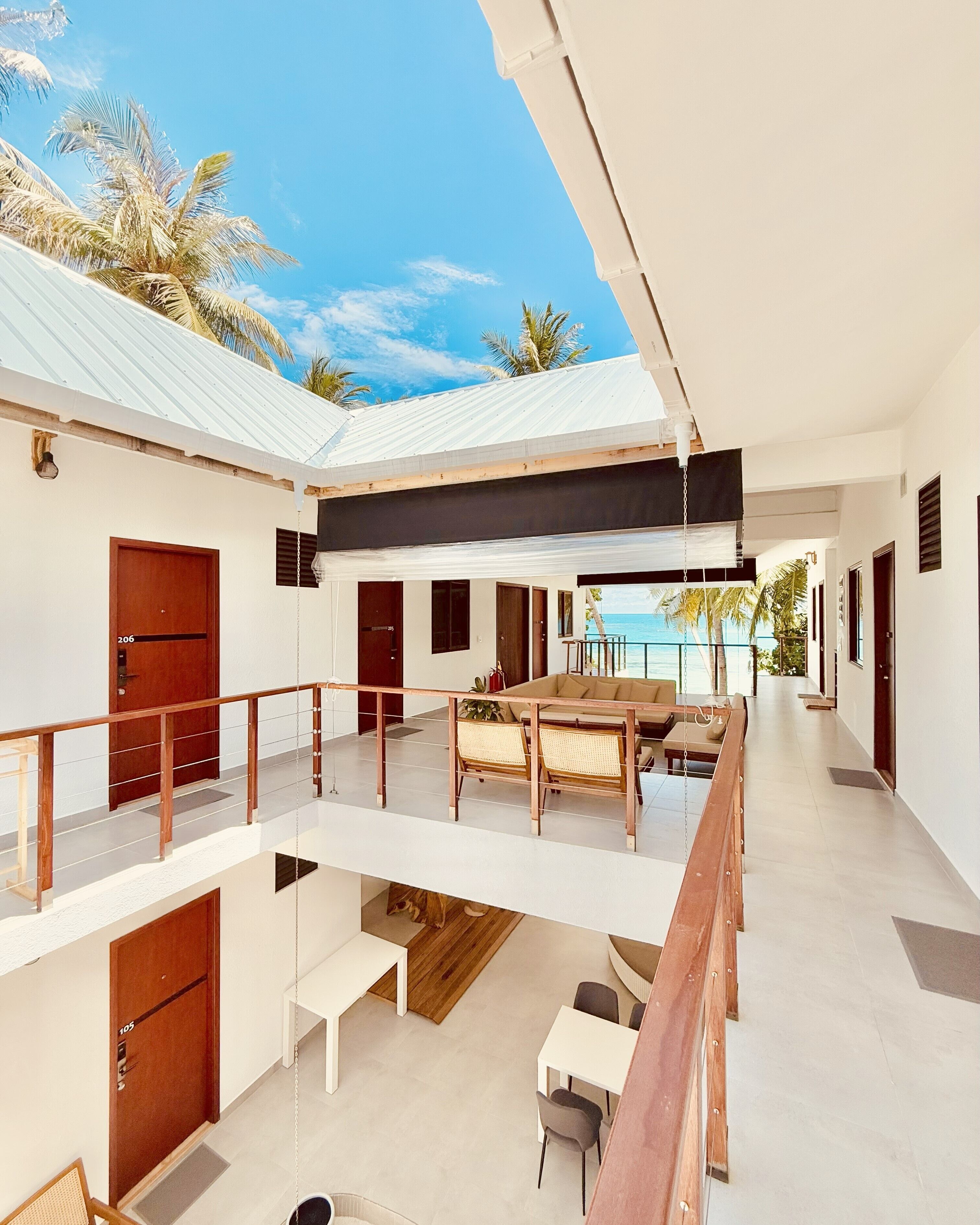 A modern multi-level building with a covered outdoor seating area, multiple doors, and a view of the sea.