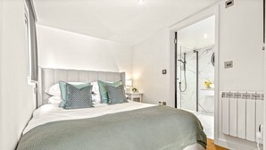 A modern bedroom with a large bed, a bedside table, a nightstand, and a glass shower enclosure. - River cabin & Mills Cottage (Henley-On-Thames)