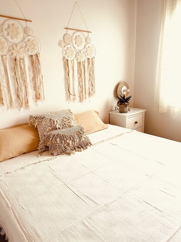 A bedroom with a large bed, a bedside table with a plant, and wall decorations.