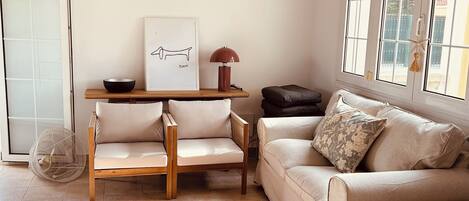 Een woonkamer met een bank, twee stoelen, een salontafel, een vloerkleed, een hanglamp en een raam met uitzicht.