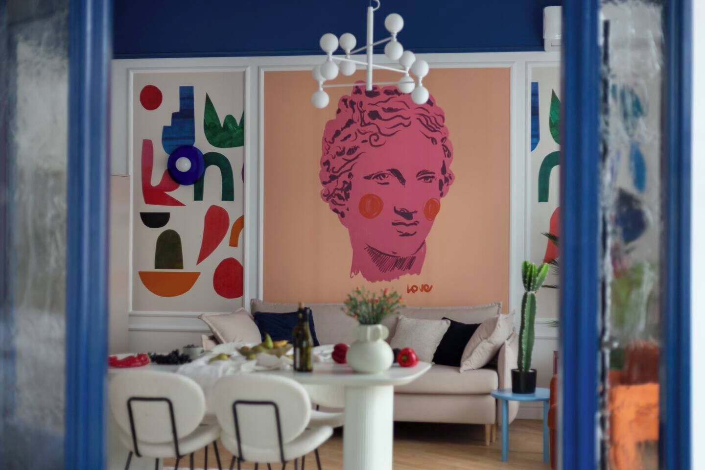 A modern living room with a white sofa, a dining table with chairs, and abstract wall art.