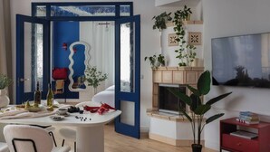 Ein modernes Wohnzimmer mit Kamin, einem Esstisch mit Früchten und einem Spiegel, sowie einem Fernseher an der Wand.