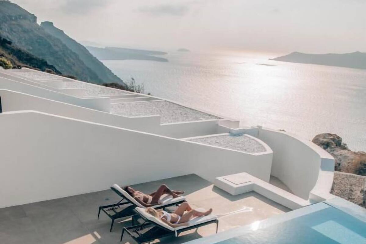 An infinity pool with two lounge chairs and a person lying on one of the chairs.