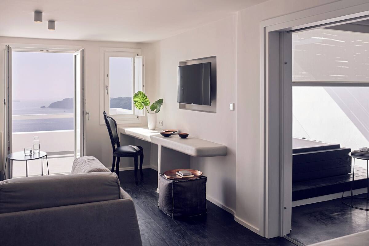 A modern living room with a sofa, a coffee table, a TV mounted on the wall, and a view of the ocean through large windows.