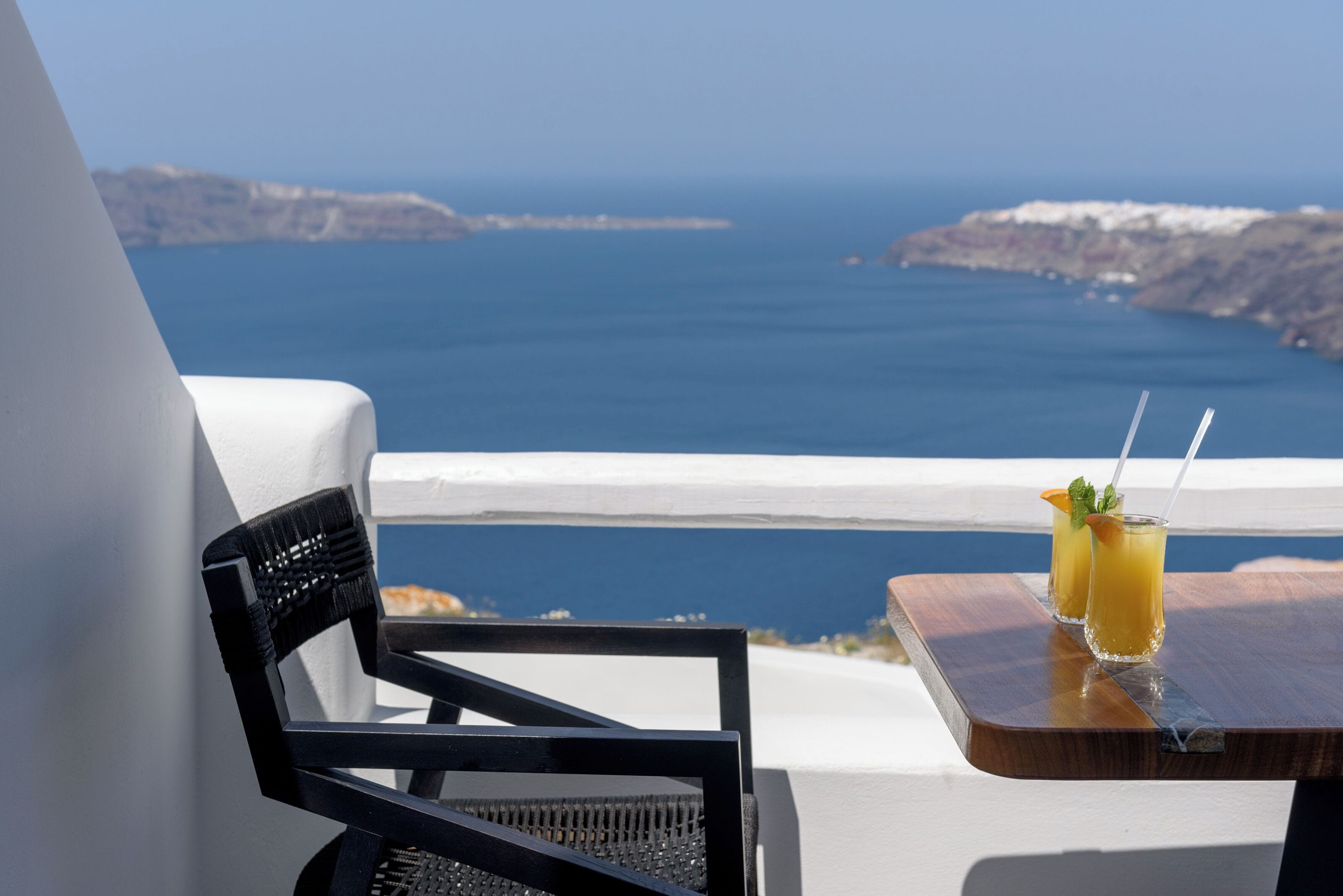 A balcony with a view of the sea, two drinks on a table, and a black chair.