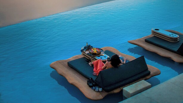 Ein Infinity-Pool mit Sonnenuntergangsblick, Liegestühlen und einer entspannten Person.