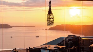 Ein Restaurant mit Blick auf den Sonnenuntergang über dem Meer, mit Tischen und Stühlen für die Essenszeit eingerichtet.