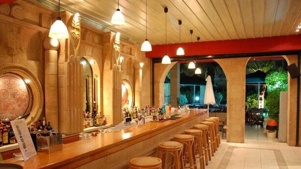 Un espace bar doté d’un long comptoir, de nombreux tabourets et de luminaires suspendus.