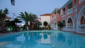 Une piscine dont l’eau est si claire qu’elle reflète parfaitement l’environnement, entourée de palmiers et bordée d’un bâtiment doté de balcons en arc de cercle.