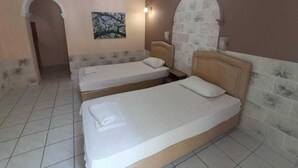 Une chambre d’hôtel avec deux lits simples, un sol carrelé, un tableau au mur et une arche en pierre.