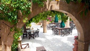 Un espace extérieur aménagé en terrasse, avec des arches en pierre, des tables et des chaises en bois.