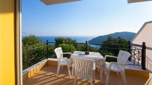 A balcony with a table and chairs, overlooking a scenic view of the sea and hills.