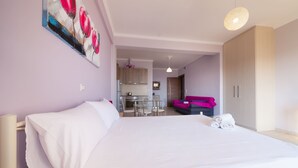 Une chambre d’hôtel comprenant un lit, un coin repas et une cuisine visible à travers une porte ouverte.