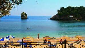 Une plage avec des parasols, des chaises et un affleurement rocheux dans l’eau.