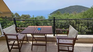 Une table et des chaises en bois sur un balcon offrant une vue sur la mer et les collines.